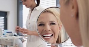 Woman with blonde hair smiles in mirror to reveal her same-day crowns